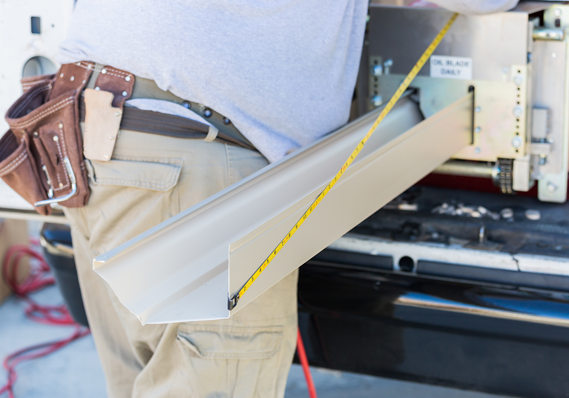 Worker Measuring An Aluminum Rain Gutter Feeding Through Seamless Shaping Machine.